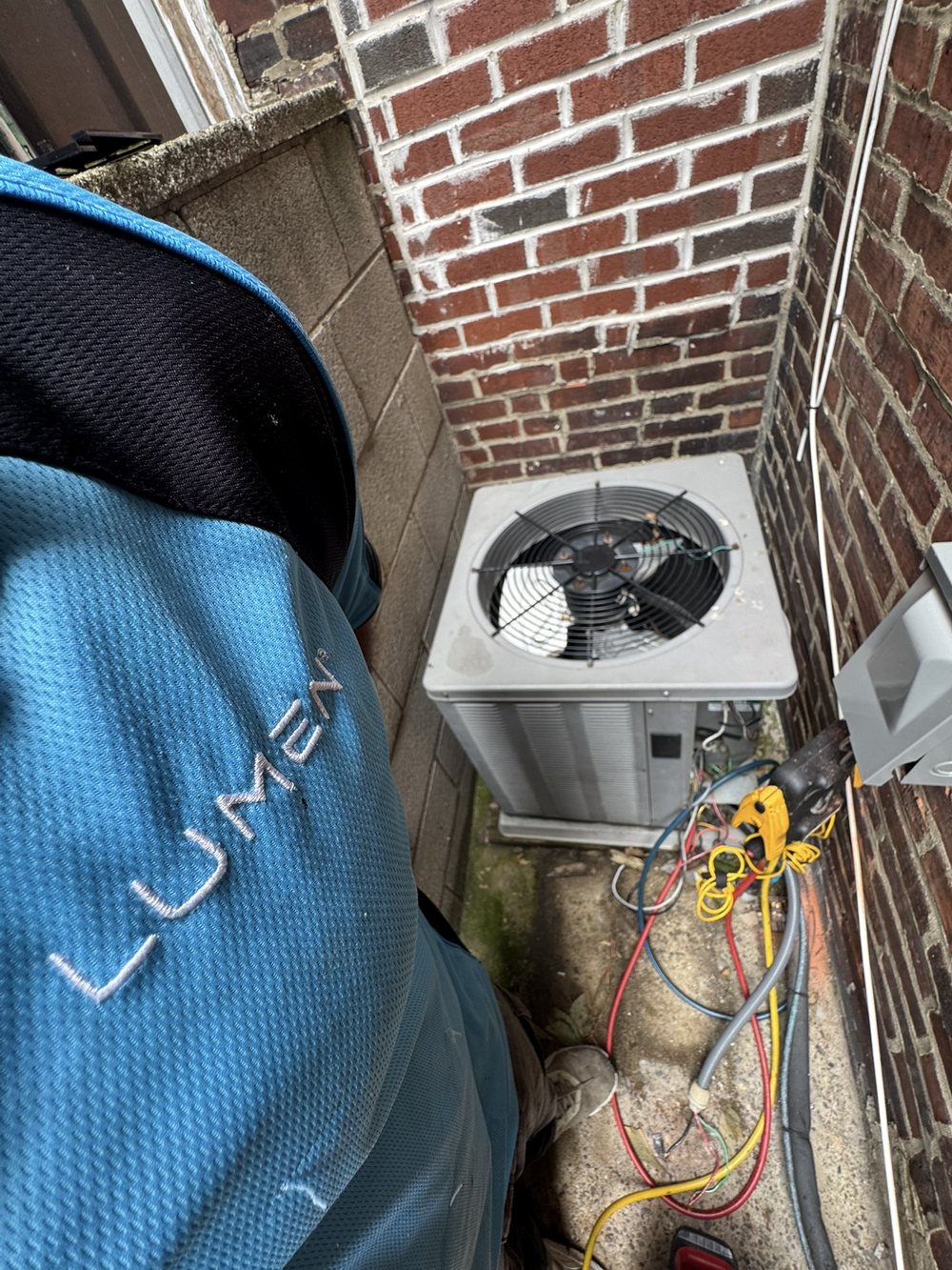 Lumen Heating and Cooling technician in a branded Lumen shirt servicing an outdoor AC condenser