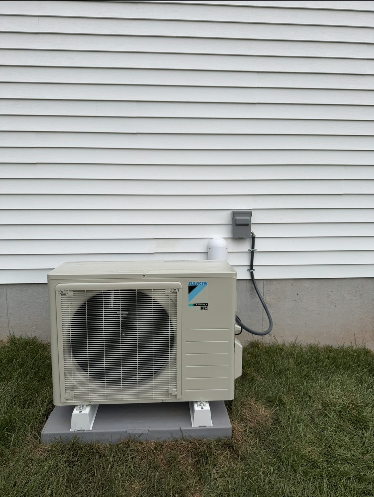 Daikin mini-split heat pump outdoor unit on a pad beside a vinyl-sided home by Lumen Heating and Cooling