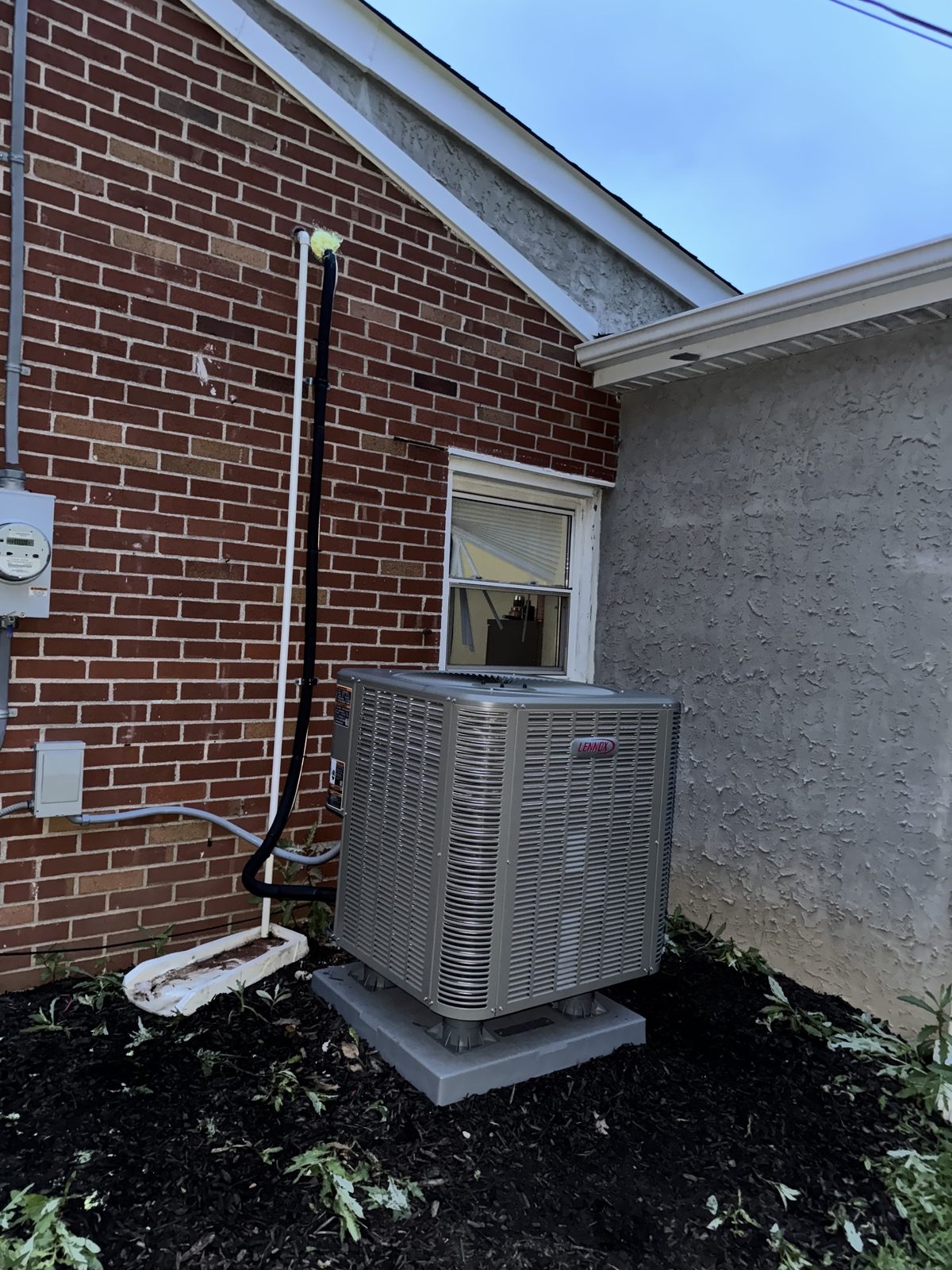 New Lennox air conditioning condenser installed beside a brick Philadelphia-area home by Lumen Heating and Cooling