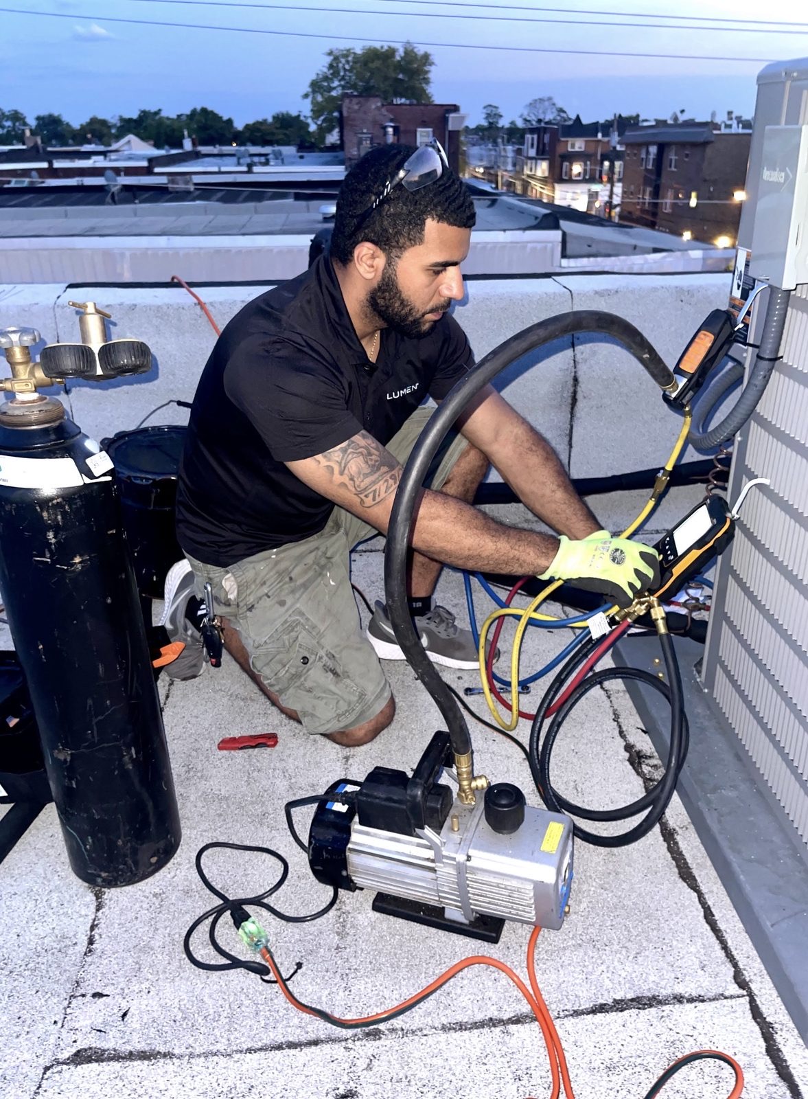 Lumen Heating and Cooling technician recovering refrigerant on a commercial rooftop at dusk