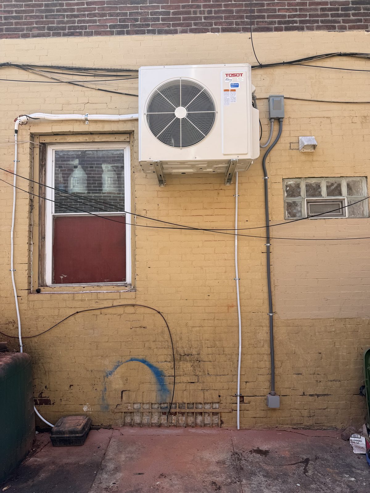 Mini-split outdoor unit wall-mounted on the brick exterior of a commercial building by Lumen Heating and Cooling