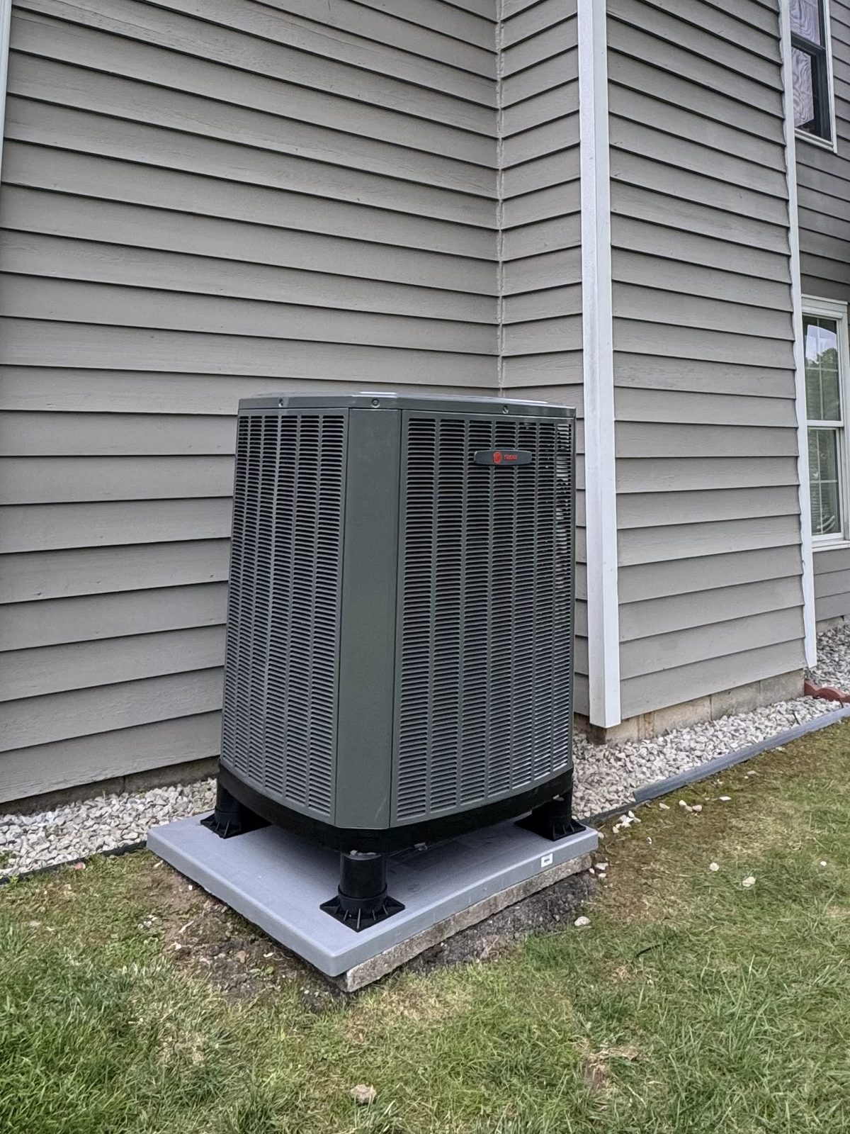 Trane heat pump outdoor unit installed on a composite pad beside a sided home by Lumen Heating and Cooling